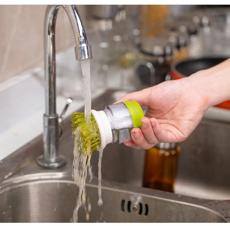 Person using a green kitchen brush with soap to clean a sink
